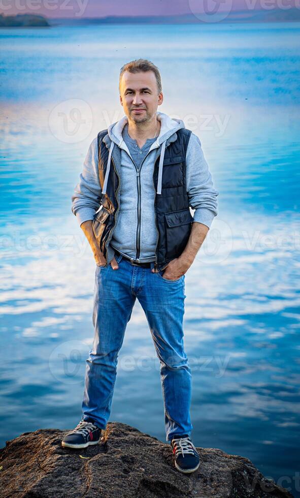 hombre en pie en rock por el agua. un hombre en pie en parte superior de un rock siguiente a un cuerpo de agua foto