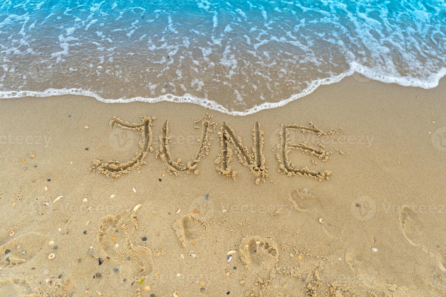 The word June is written on the sand of a beach by the sea. Washed off by a wave. The inscription disappears. End of summer concept. Back to school. photo