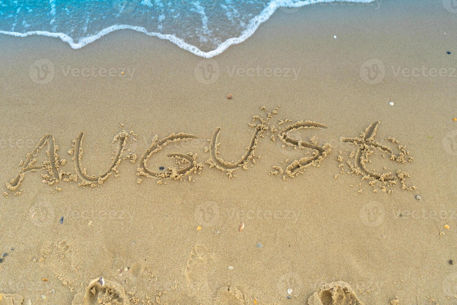 The word August is written on the sand of a beach by the sea. Washed off by a wave. The inscription disappears. End of summer concept. Back to school. photo