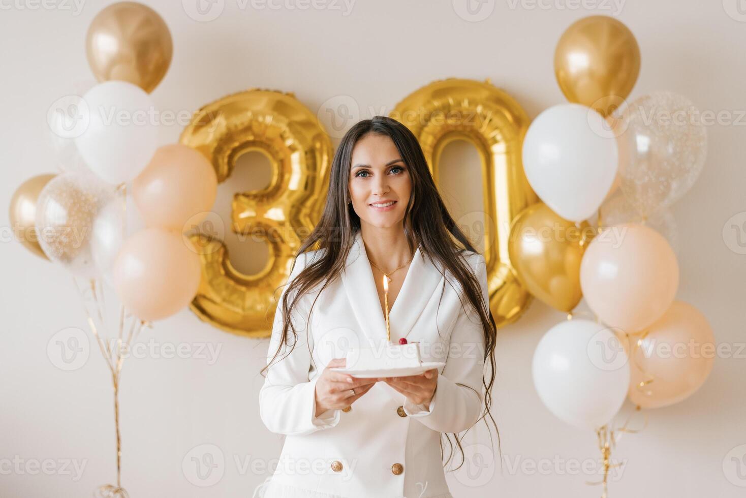 Young caucasian woman holding a birthday cake with a candle in a stylish white dress with feathers photo