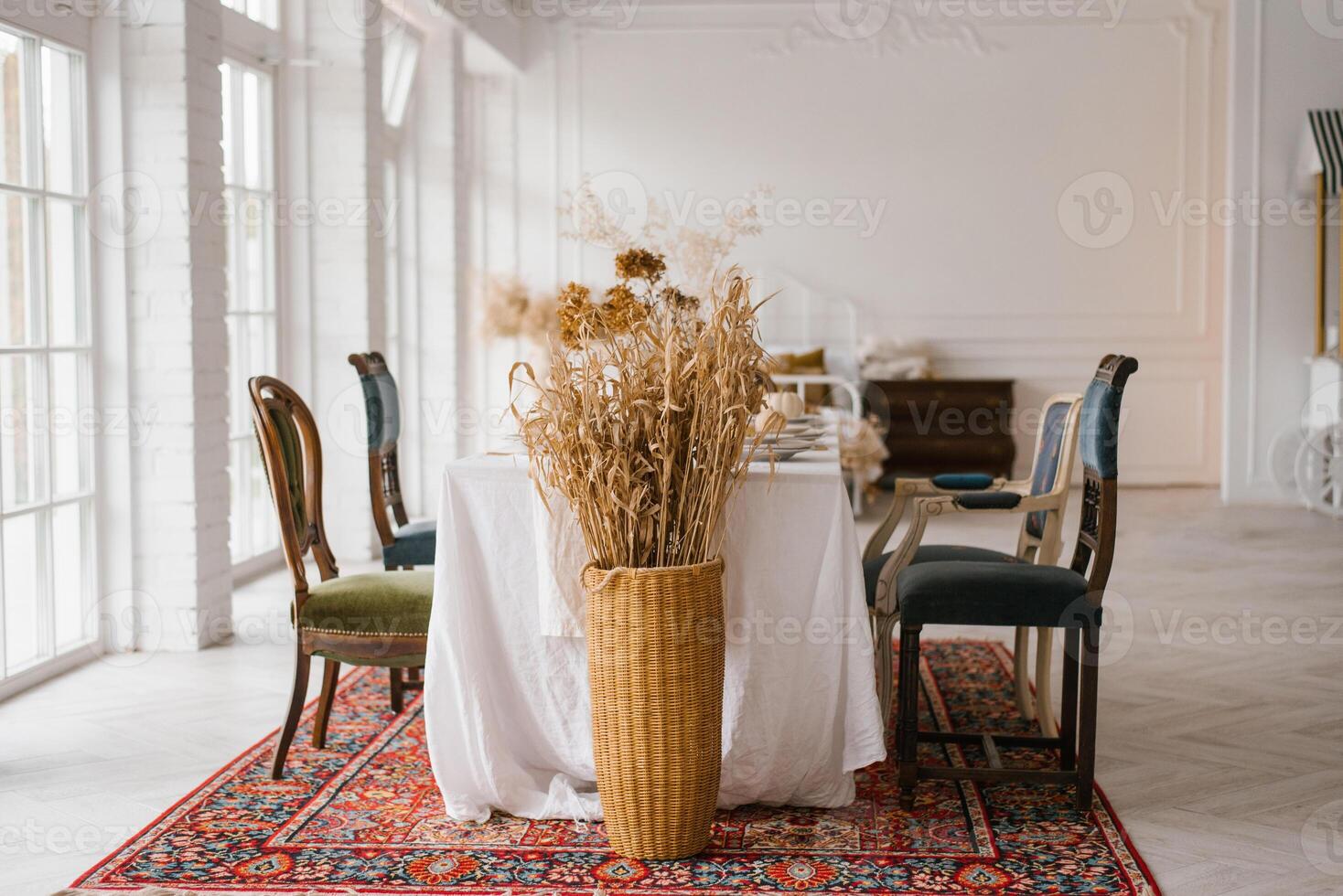 Table set for Thanksgiving with vintage chairs of different shapes and colors in a bright living room with French windows photo