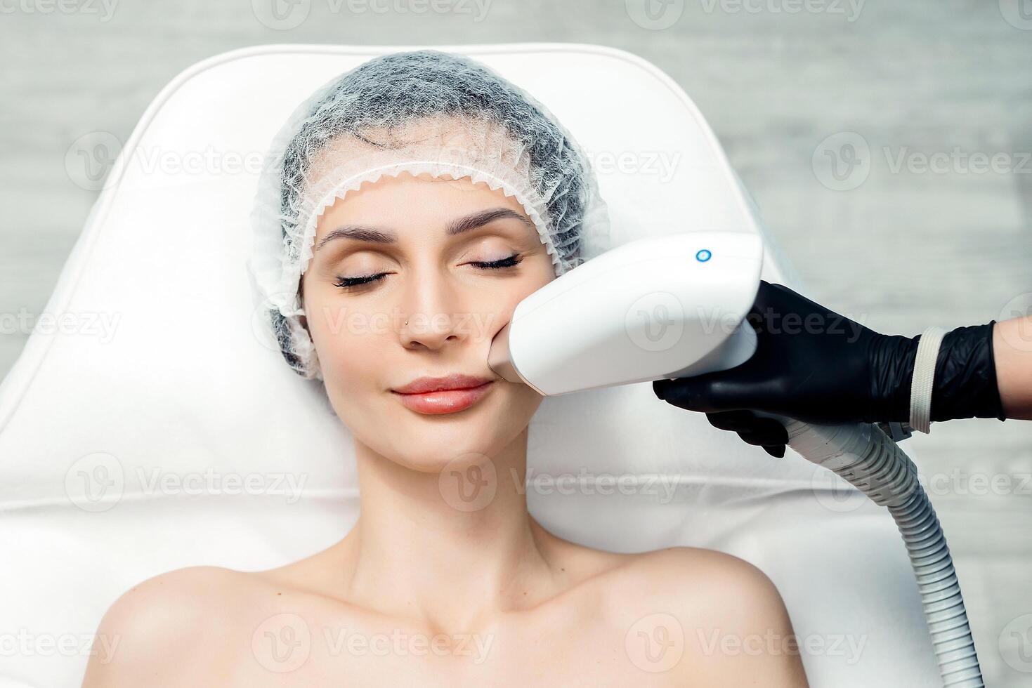 Body care concept. Laser hair removal. Young Caucasian woman lies on the sofa, female cosmetologist doing laser face hair removal in a beauty salon. Girl on mustache laser hair removal procedure. photo