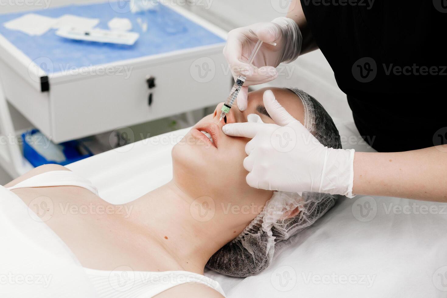 Surgeon, in medical gloves, carefully and slowly injects hyaluronic acid into woman's lips with a syringe. lip augmentation procedure. beauty injections. Plastic surgery. photo