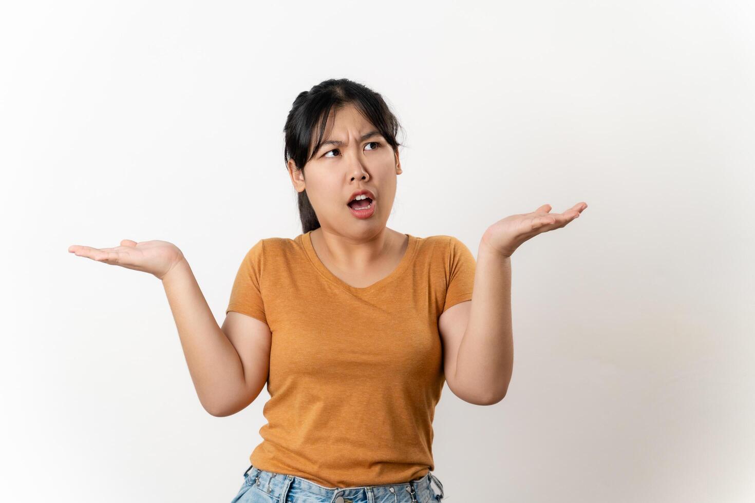 The confused beautiful Asian woman shrugging shoulders spreads hands sideways standing on white background. bewilderment, doubting, have no idea, don't know. photo