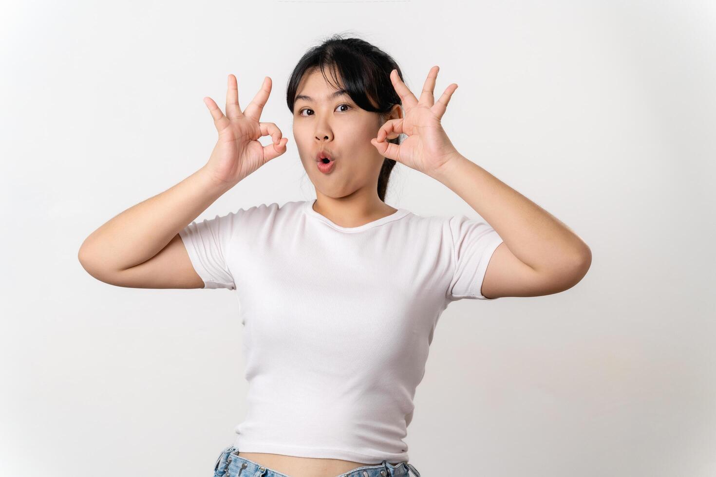 The cheerful young Asian woman smiling and showing the OK hand sign standing on white background. photo