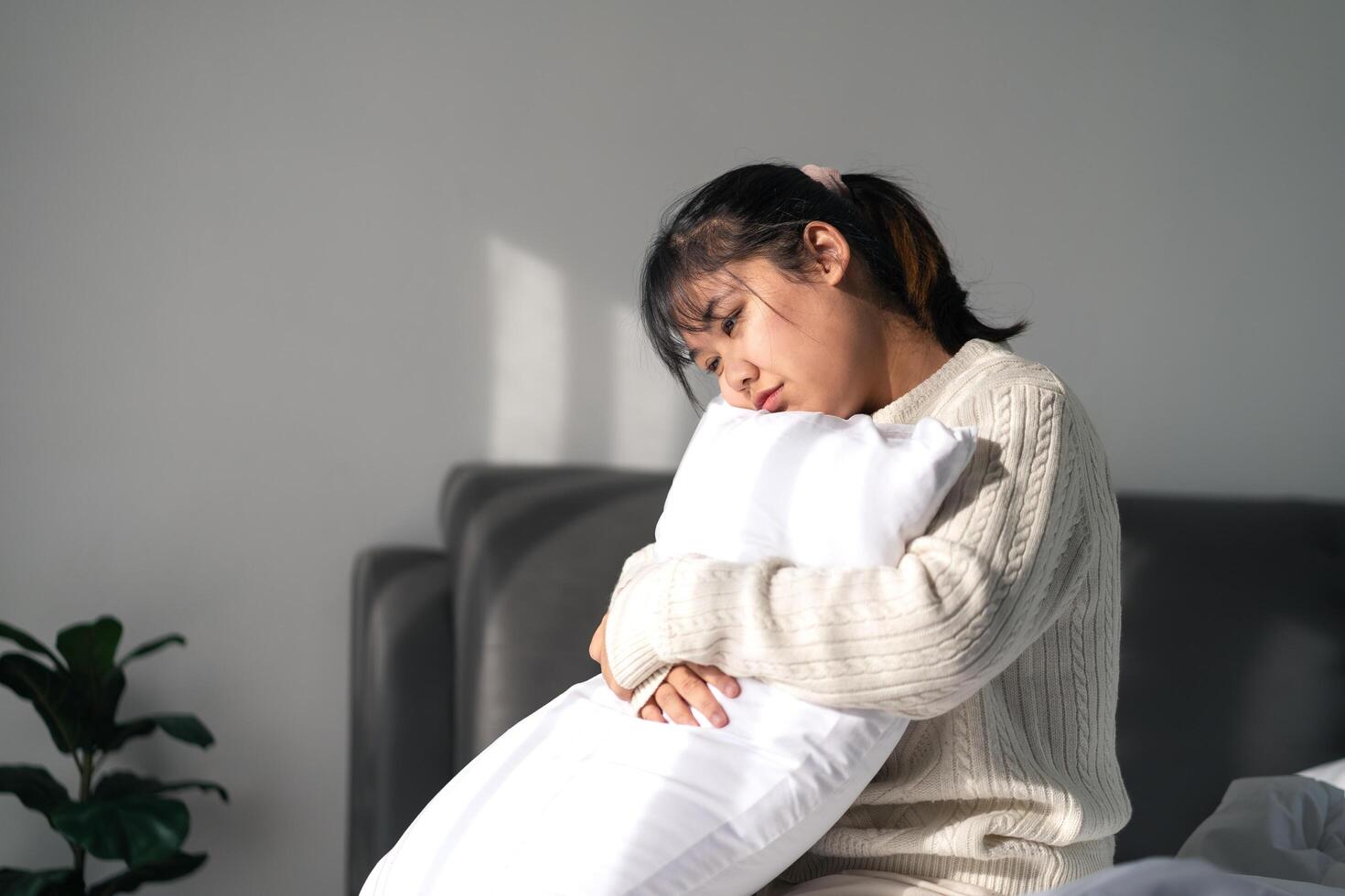 The sad and lonely woman is hugging a pillow on the bed in the bedroom at home. photo