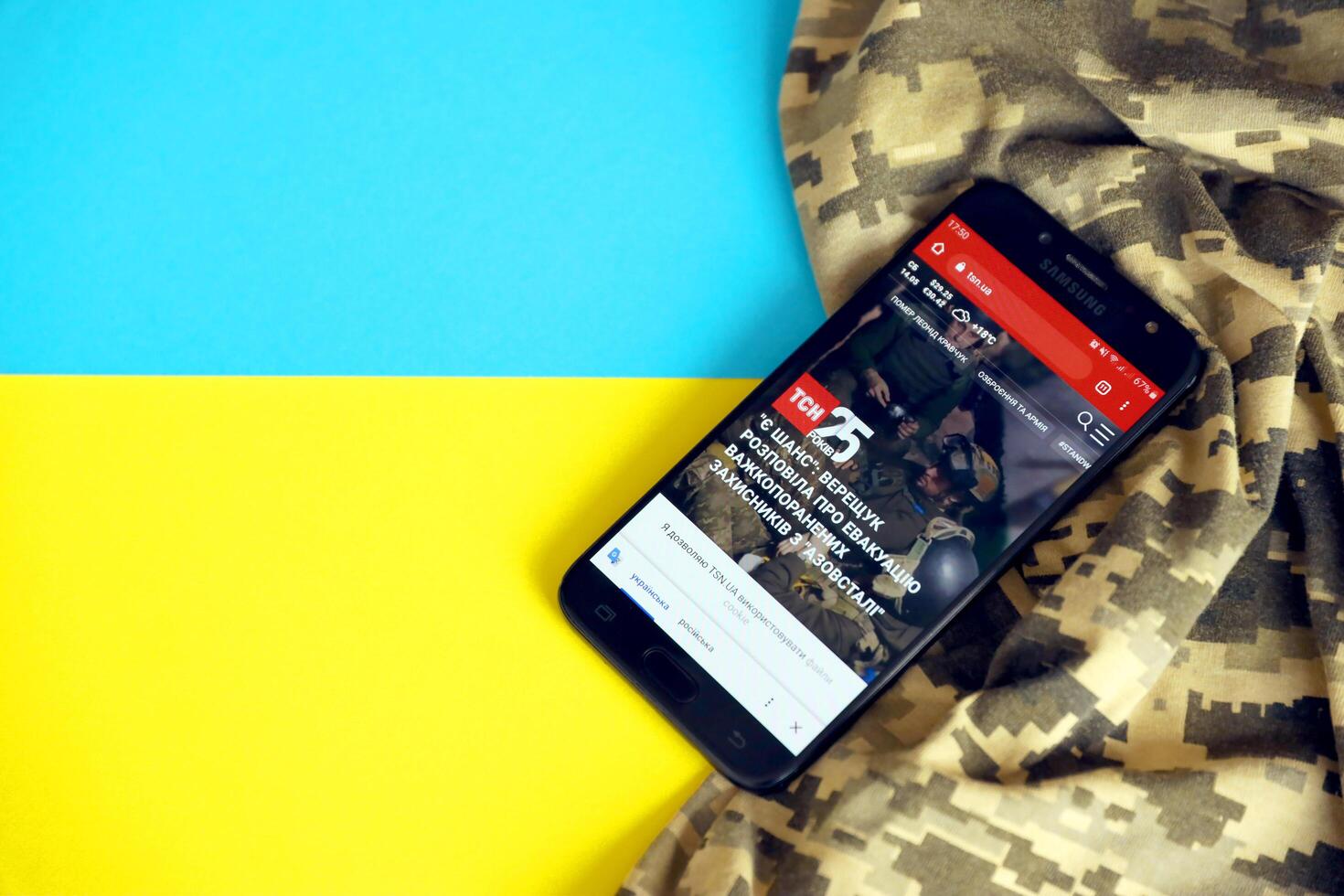 KYIV, UKRAINE - 4 MAY, 2023 TSN ukrainian news portal on smartphone screen with ukrainian flag and camouflage fabric photo