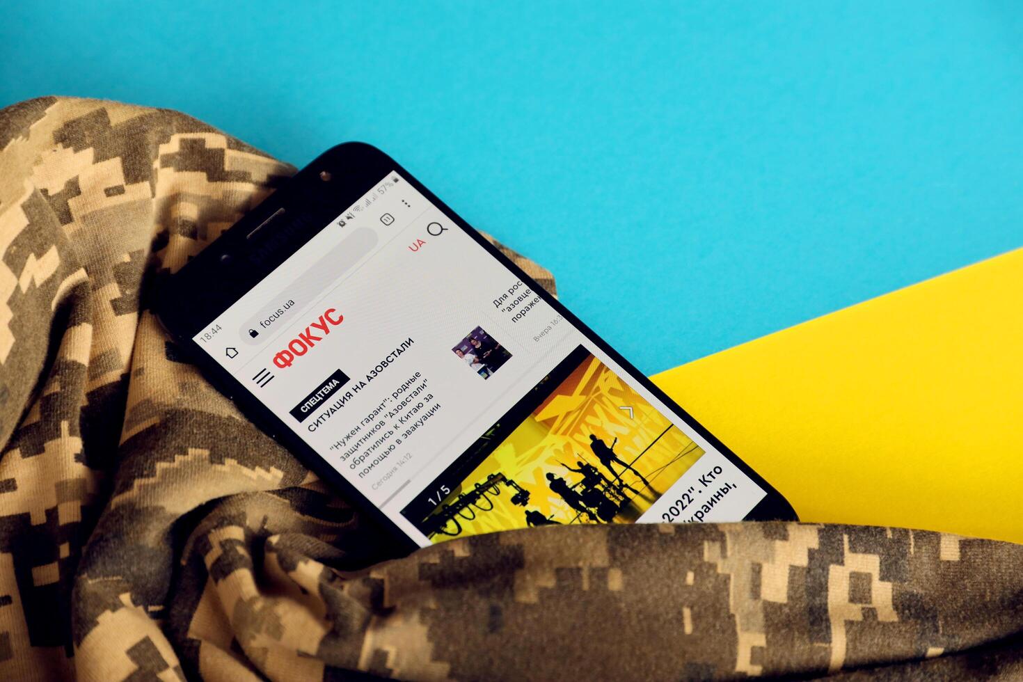 KYIV, UKRAINE - 4 MAY, 2023 Focus ukrainian news portal on smartphone screen with ukrainian flag and camouflage fabric photo