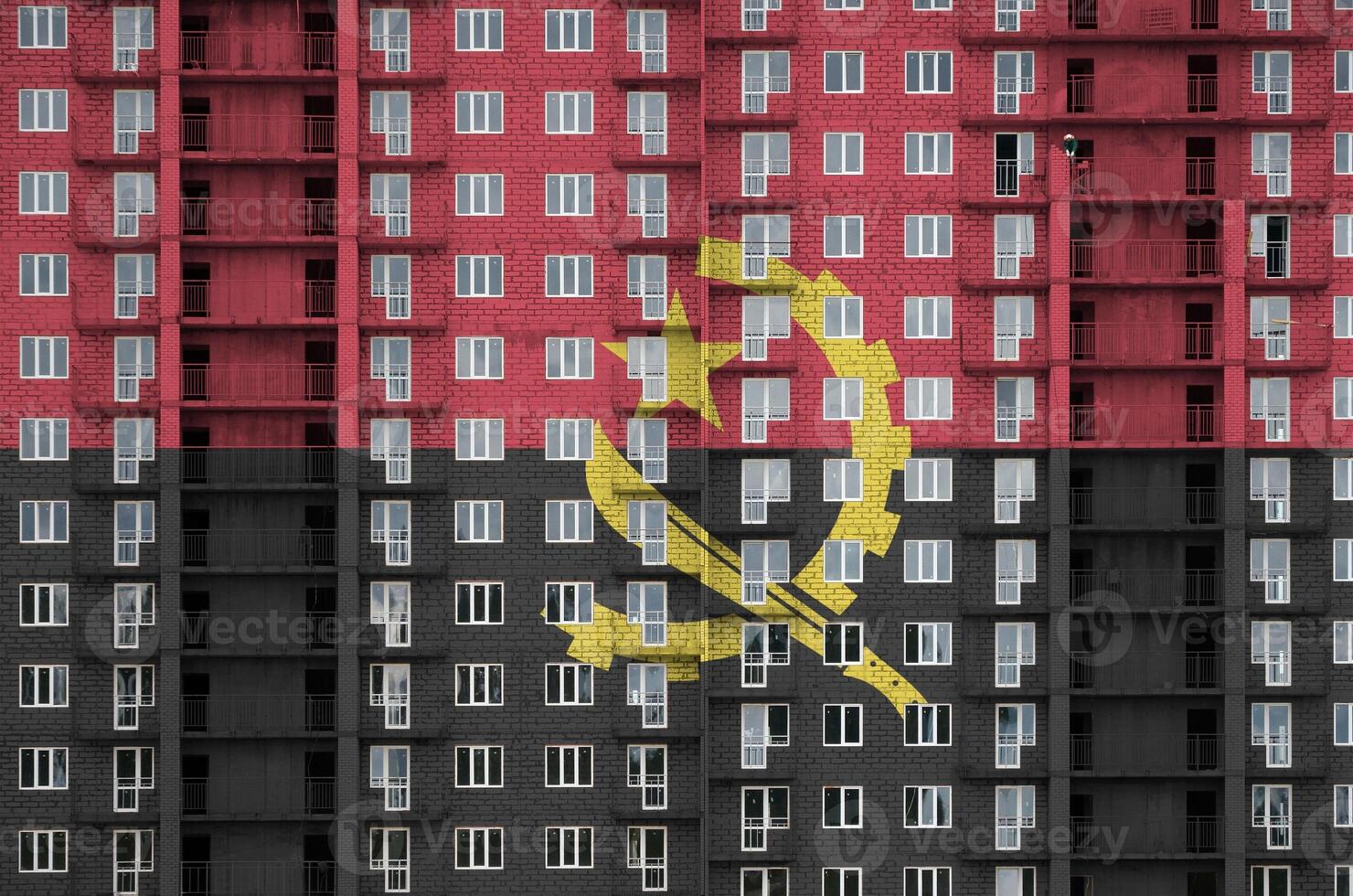 Angola flag depicted in paint colors on multi-storey residental building under construction. Textured banner on brick wall background photo