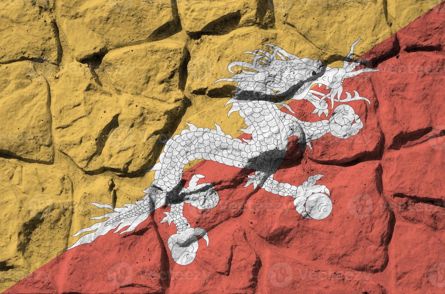 Bhutan flag depicted in paint colors on old stone wall closeup. Textured banner on rock wall background photo