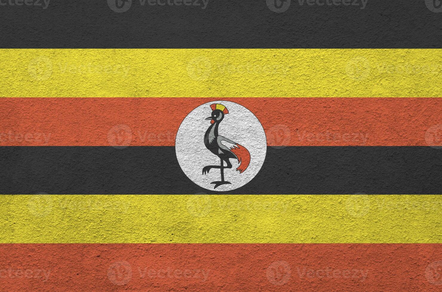 Uganda flag depicted in bright paint colors on old relief plastering wall. Textured banner on rough background photo