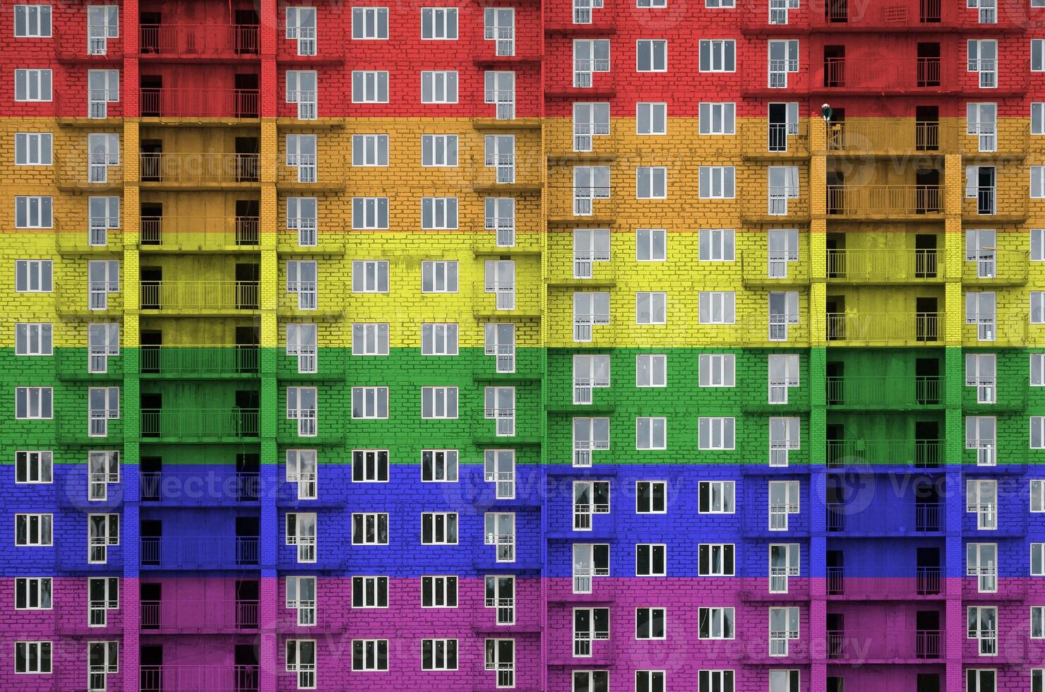 LGBT community flag depicted in paint colors on multi-storey residental building under construction. Textured banner on brick wall background photo