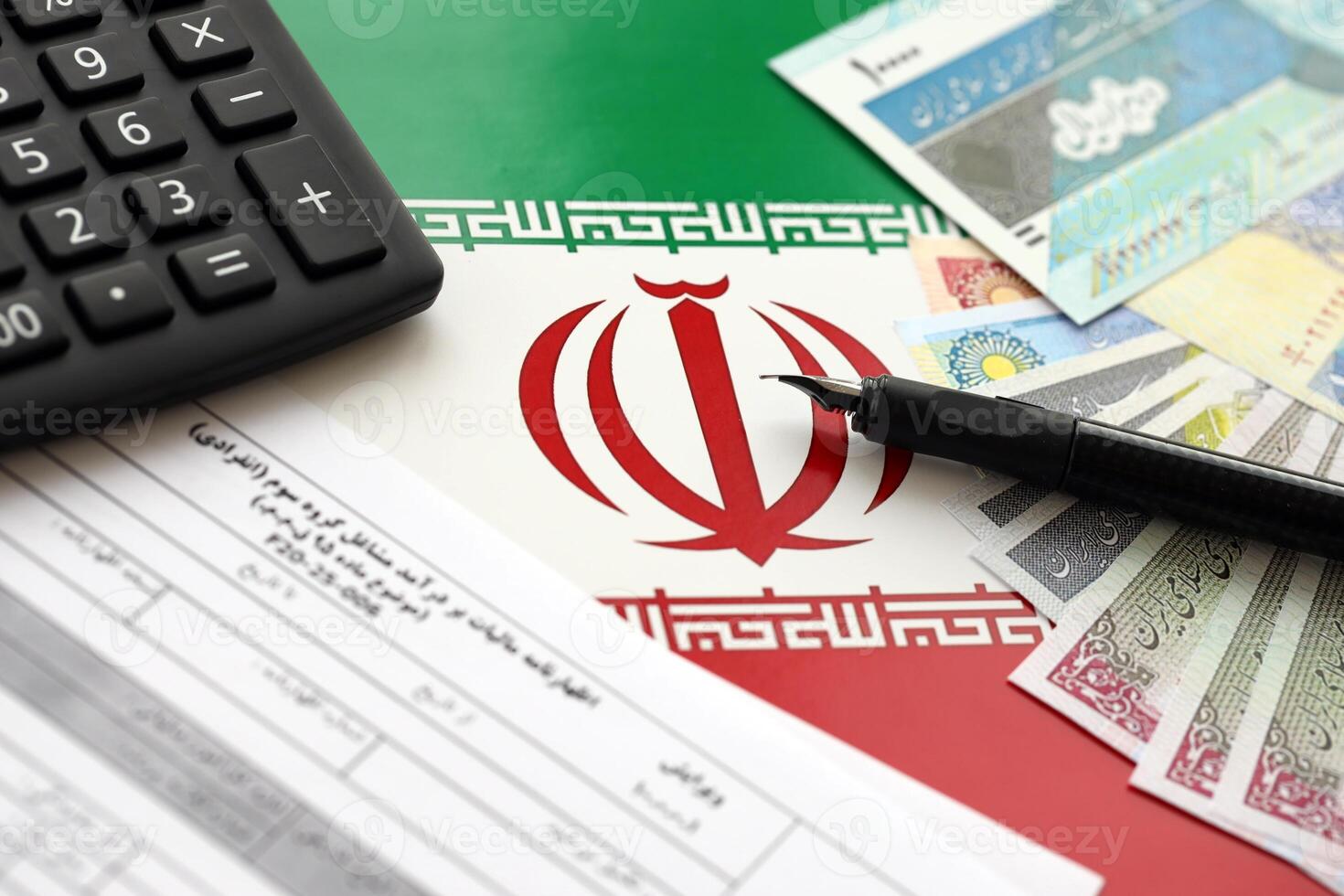 Iranian annual income tax return form F20-25-006 ready to fill on table with pen, calculator and iranian money on flag photo