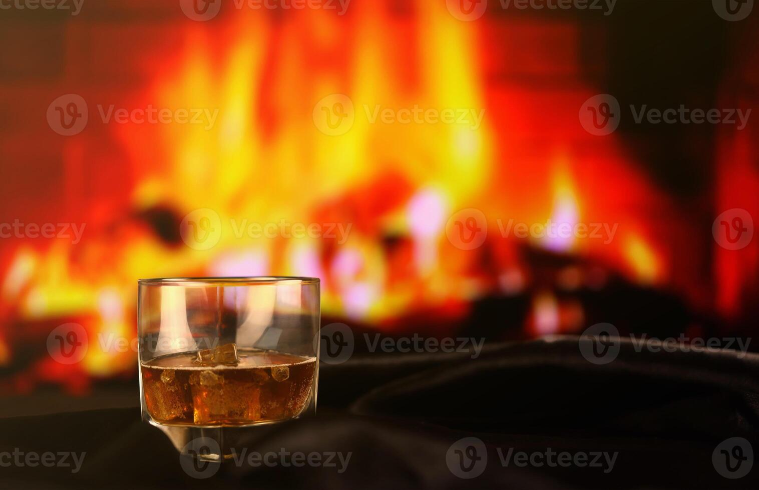 Whisky or whiskey or bourbon with ice on wooden surface on fireplace background. Luxury elite alcohol in wide glass. Low key scene photo