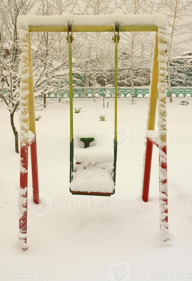 Children's swing, covered with a thick layer of snow after a heavy snowfall photo