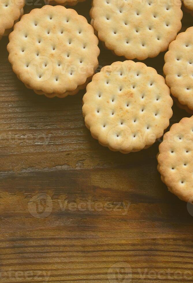 A round sandwich cookie with coconut filling lies in large quantities on a brown wooden surface. Photo of edible treats on a wooden background with copy space