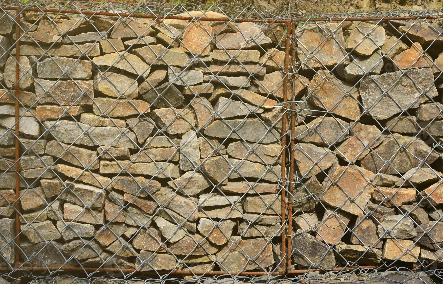Photo of several gabions. The mesh cells of the cubic form are filled with mountain stones of various shapes that let water through the rain, but protect the road from falling stones