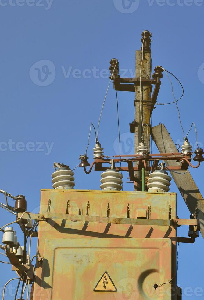 Old and obsolete electrical transformer against the background of a cloudless blue sky. Device for distribution of supply of high-voltage energy photo