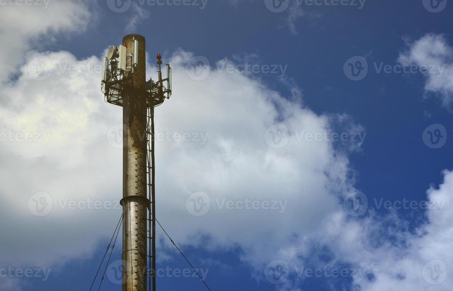 High metal chimney of industrial plant with ladder in the form of metal braces against the background of a cloudy blue sky photo