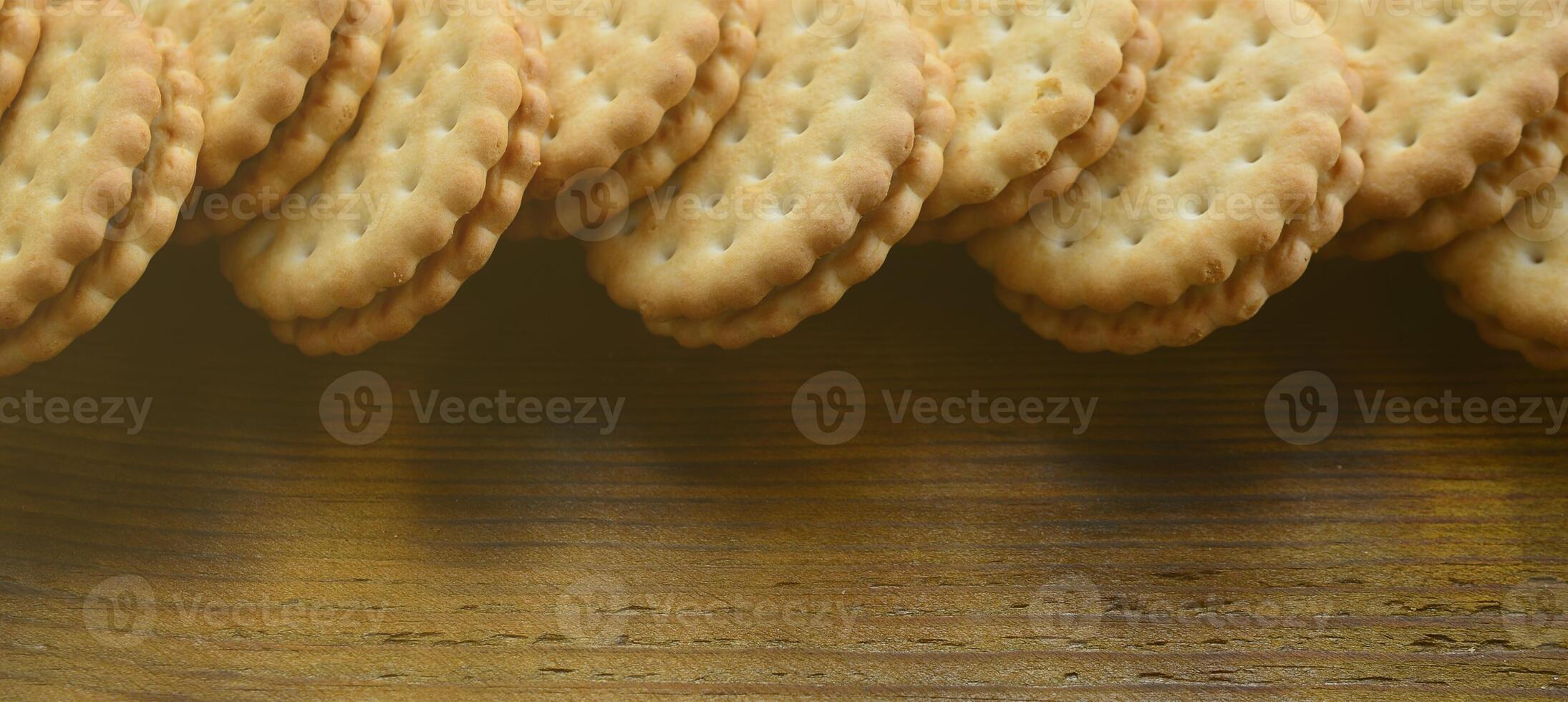 A round sandwich cookie with coconut filling lies in large quantities on a brown wooden surface. Photo of edible treats on a wooden background with copy space