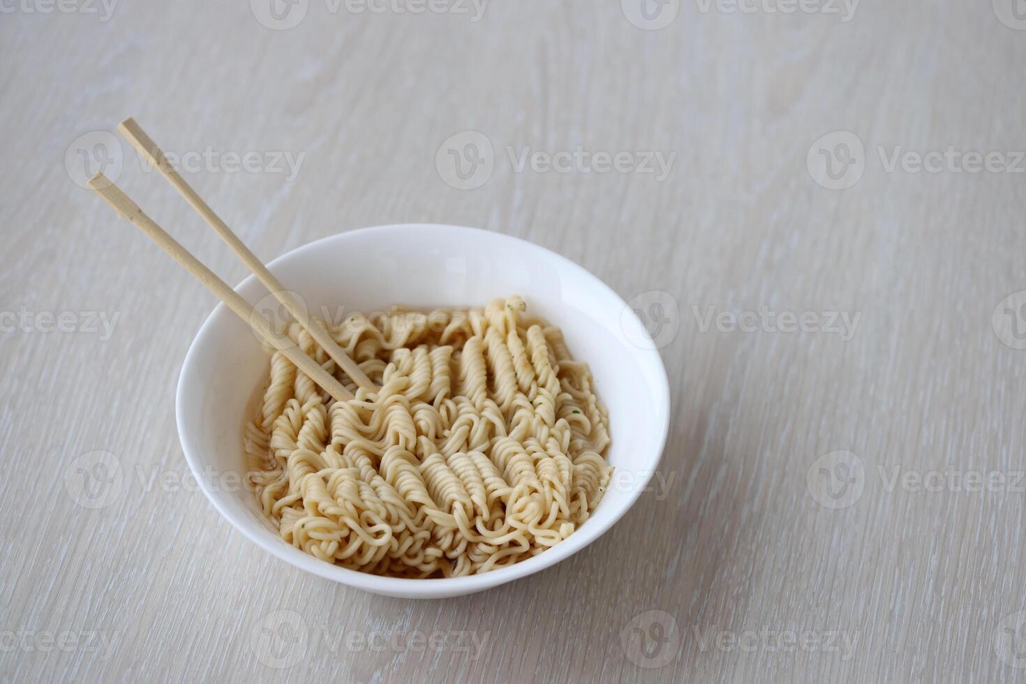 Bowl of instant cooking noodles with wooden chopsticks on white wooden table photo