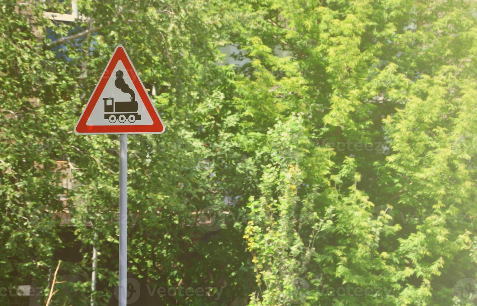 Triangular road sign with a picture of a black locomotive on a white background in a red frame. Warning sign for the presence of a railway crossing the motor road photo
