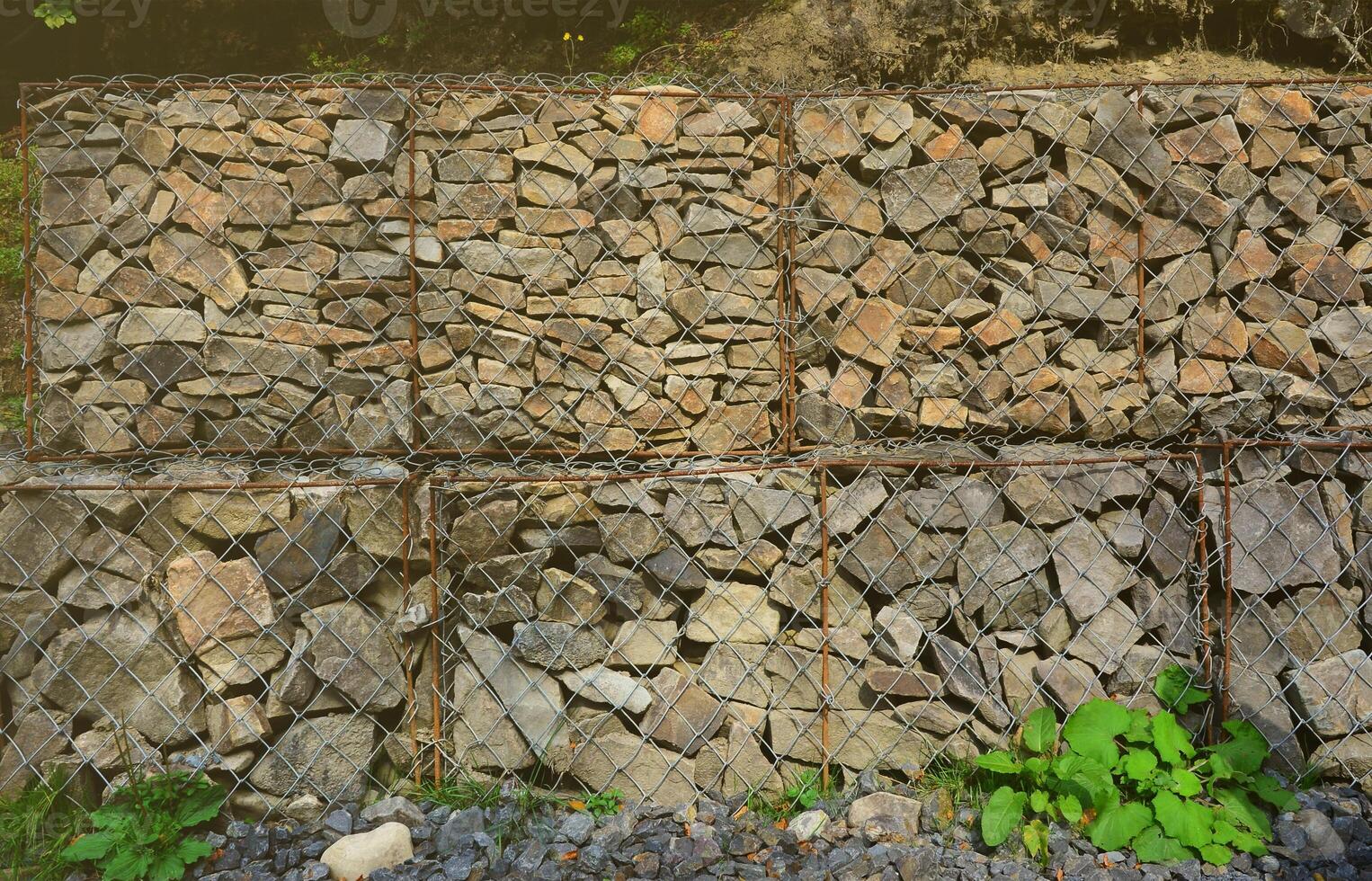 Photo of several gabions. The mesh cells of the cubic form are filled with mountain stones of various shapes that let water through the rain, but protect the road from falling stones