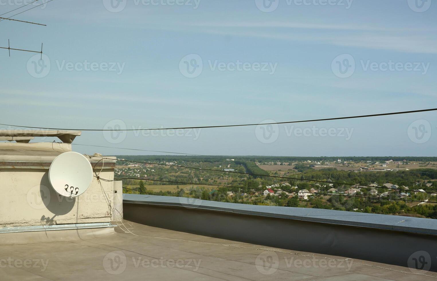 White satellite dish with three converters mounted on residental building rooftop concrete wall. Satellite television photo