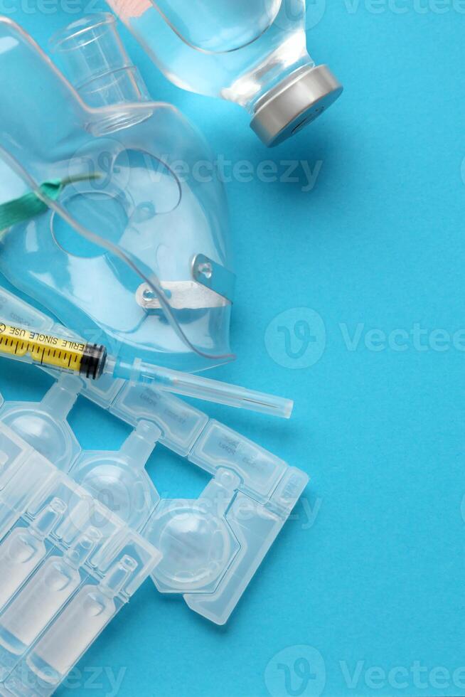 Coronavirus treatment concept. A medical face mask nebulizer for treatment of respiratory tract and packs of ampoules flat layed on blue background photo