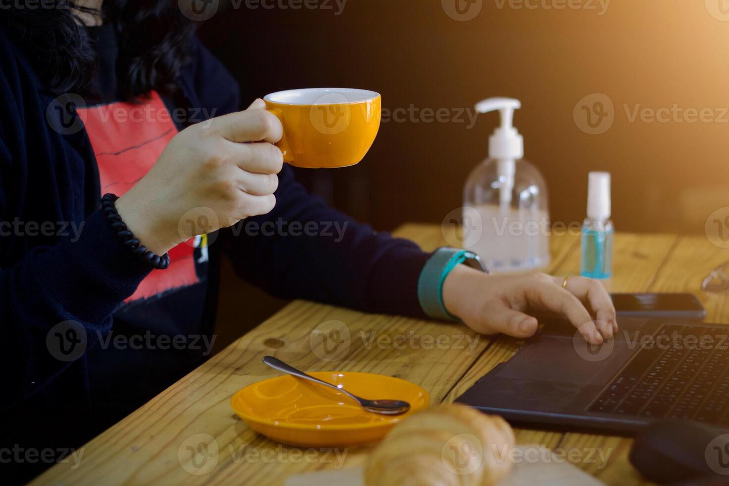 mujer utilizando ordenador portátil trabajando y limpiar manos con alcohol bebida café taza caliente a hogar foto