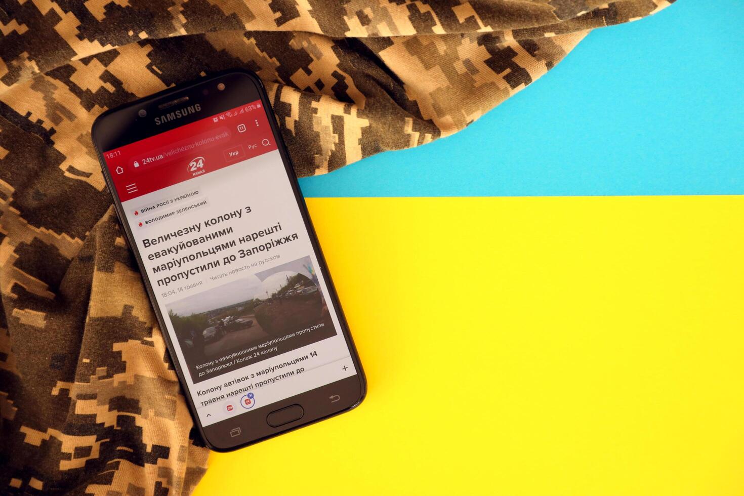 KYIV, UKRAINE - 4 MAY, 2023 24tv ukrainian news portal on smartphone screen with ukrainian flag and camouflage fabric photo