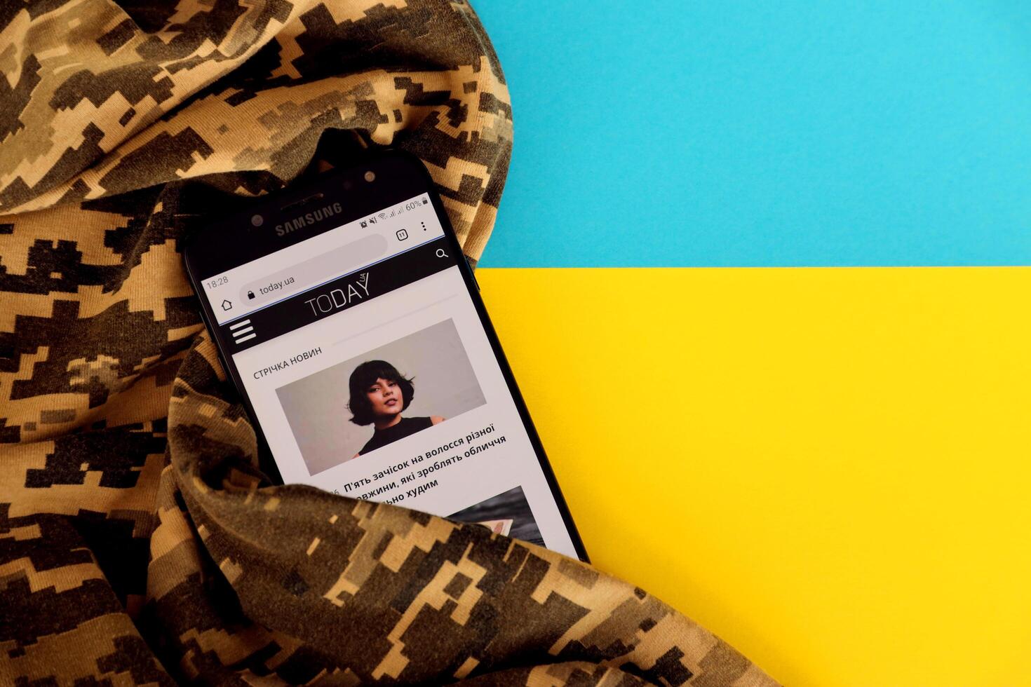 KYIV, UKRAINE - 4 MAY, 2023 Today UA ukrainian news portal on smartphone screen with ukrainian flag and camouflage fabric photo