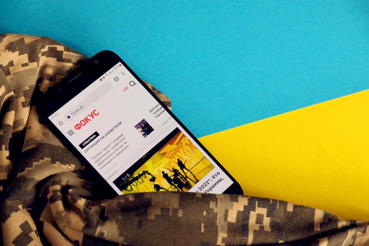KYIV, UKRAINE - 4 MAY, 2023 Focus ukrainian news portal on smartphone screen with ukrainian flag and camouflage fabric photo