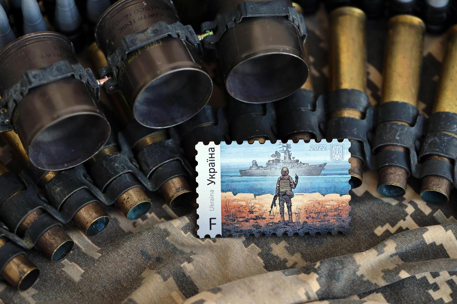 TERNOPIL, UKRAINE - SEPTEMBER 29, 2023 Famous Ukrainian postmark with russian warship and ukrainian soldier as wooden souvenir on army camouflage uniform cloth and machine gun belt photo