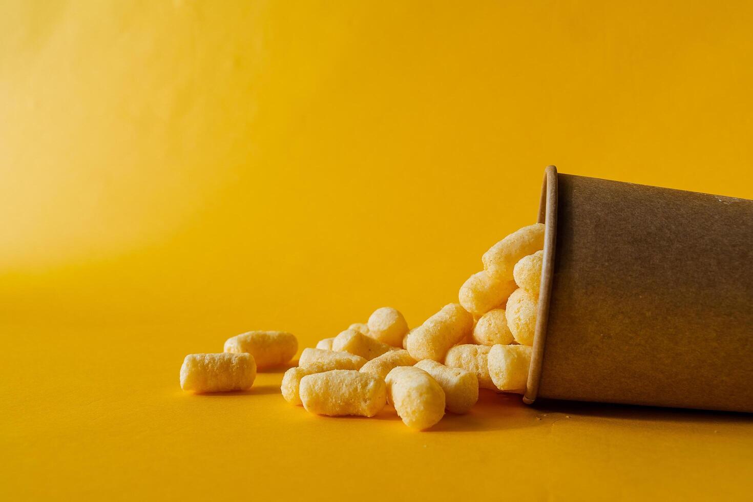 yellow corn sticks in a glass on a colored background, a full box of sweet corn sticks, a treat for children, yellow background, minimalism photo