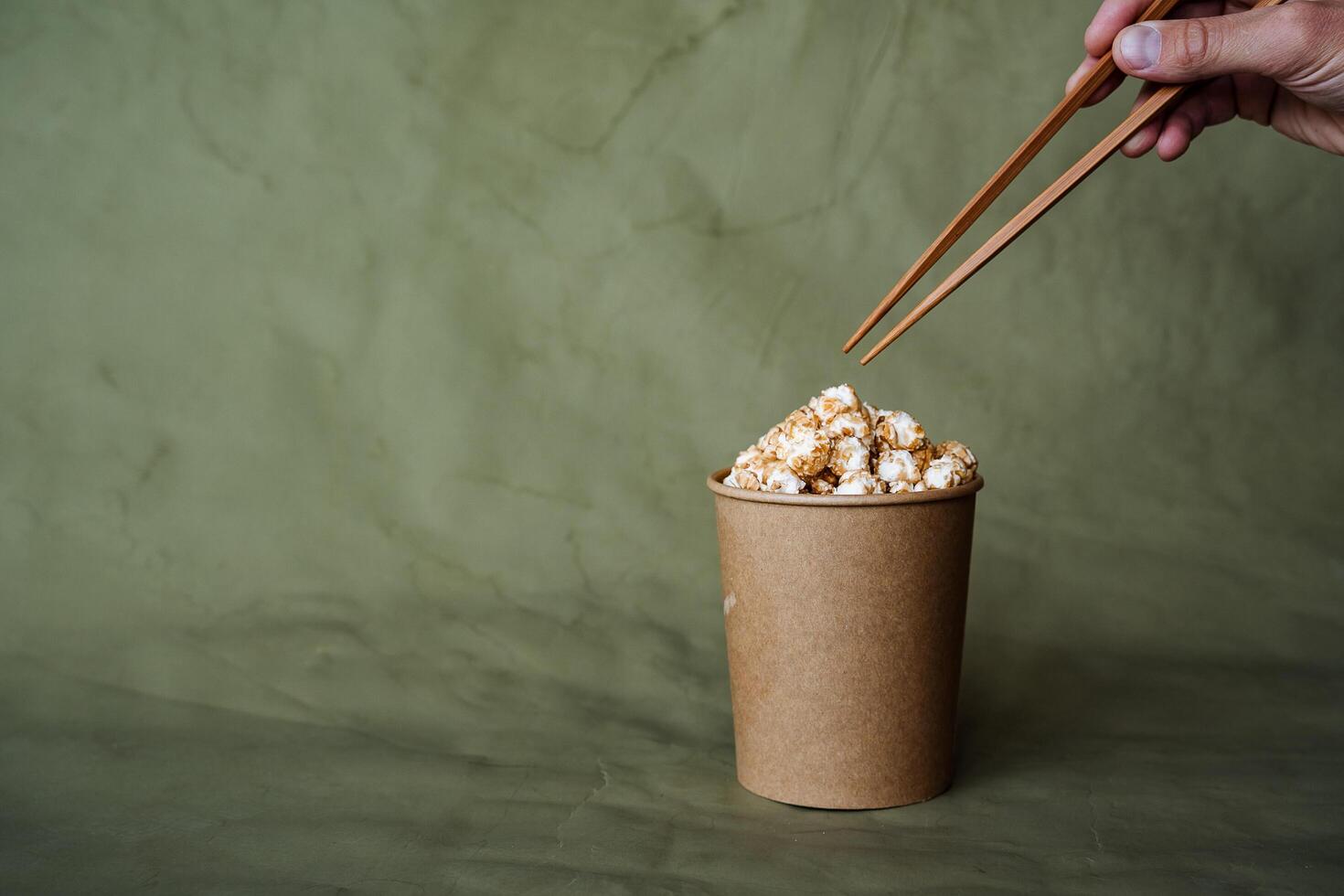 Chinese chopsticks to take popcorn from a box, a full can of popcorn, minimalistic style, on a colored background, concept picture, abstraction photo