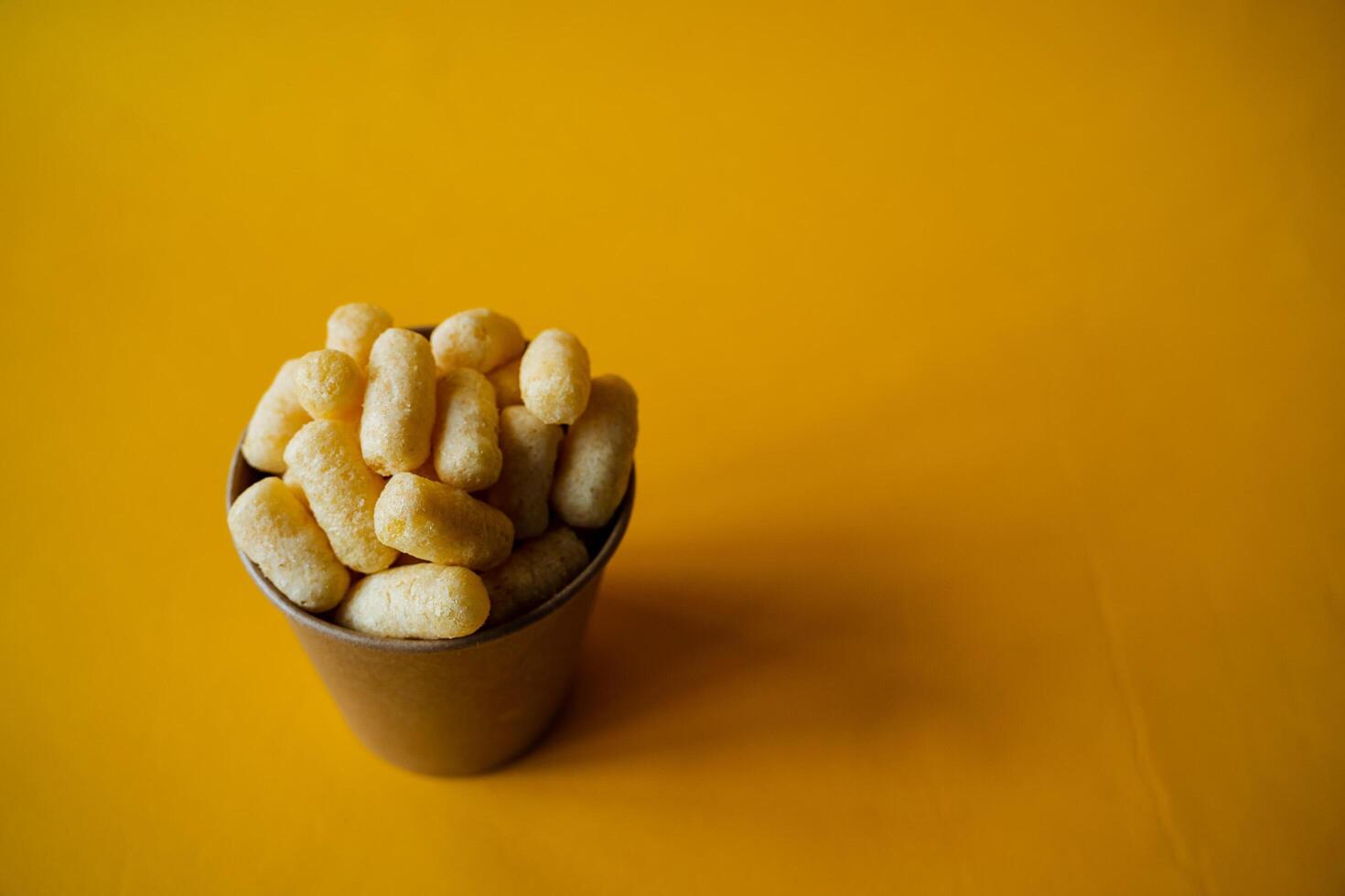 yellow corn sticks in a glass on a colored background, a full box of sweet corn sticks, a treat for children, yellow background, minimalism photo