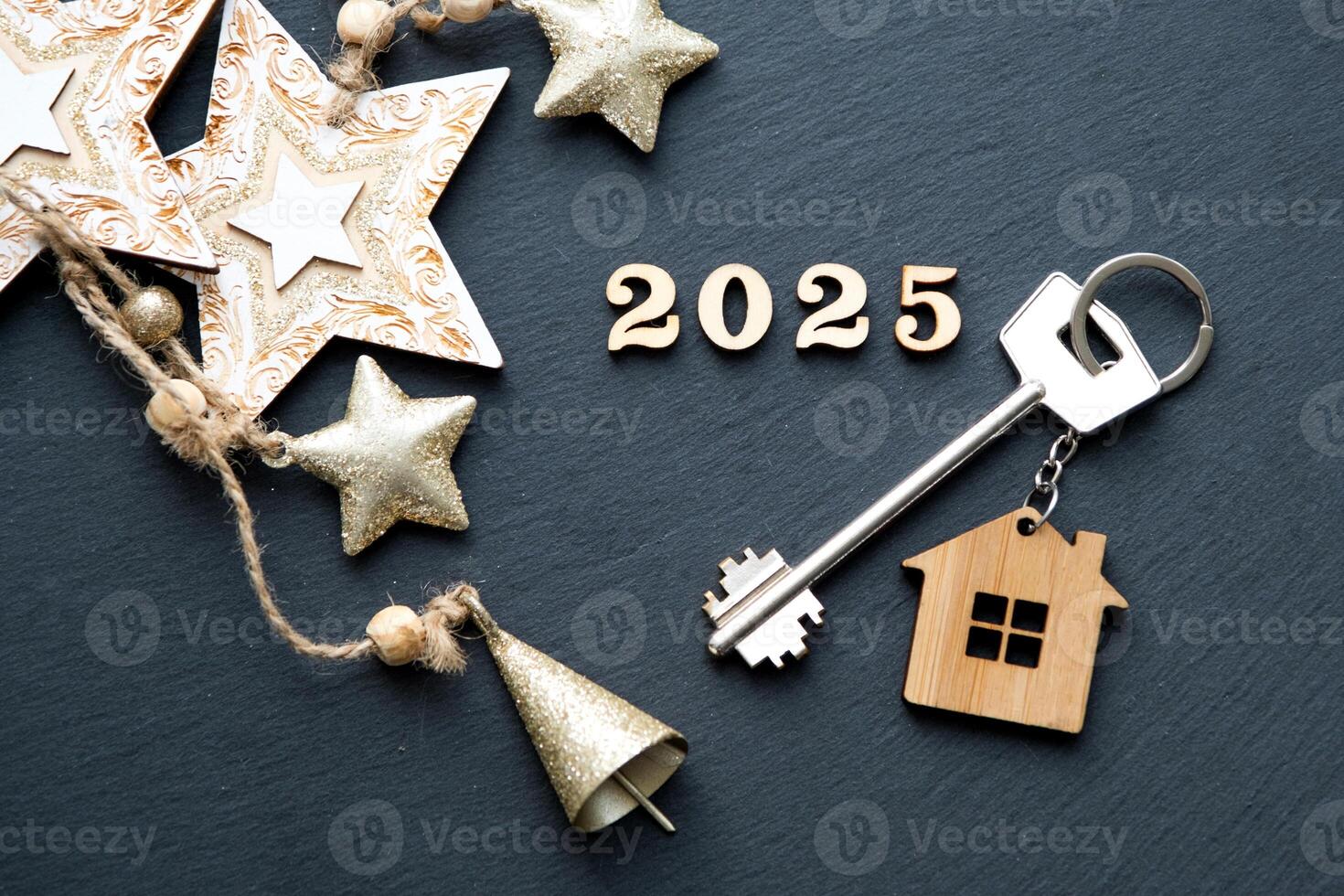 House key with keychain cottage on festive black background with stars, lights of garlands. New Year 2025 wooden letters, greeting card. Purchase, construction, relocation, mortgage, insurance photo