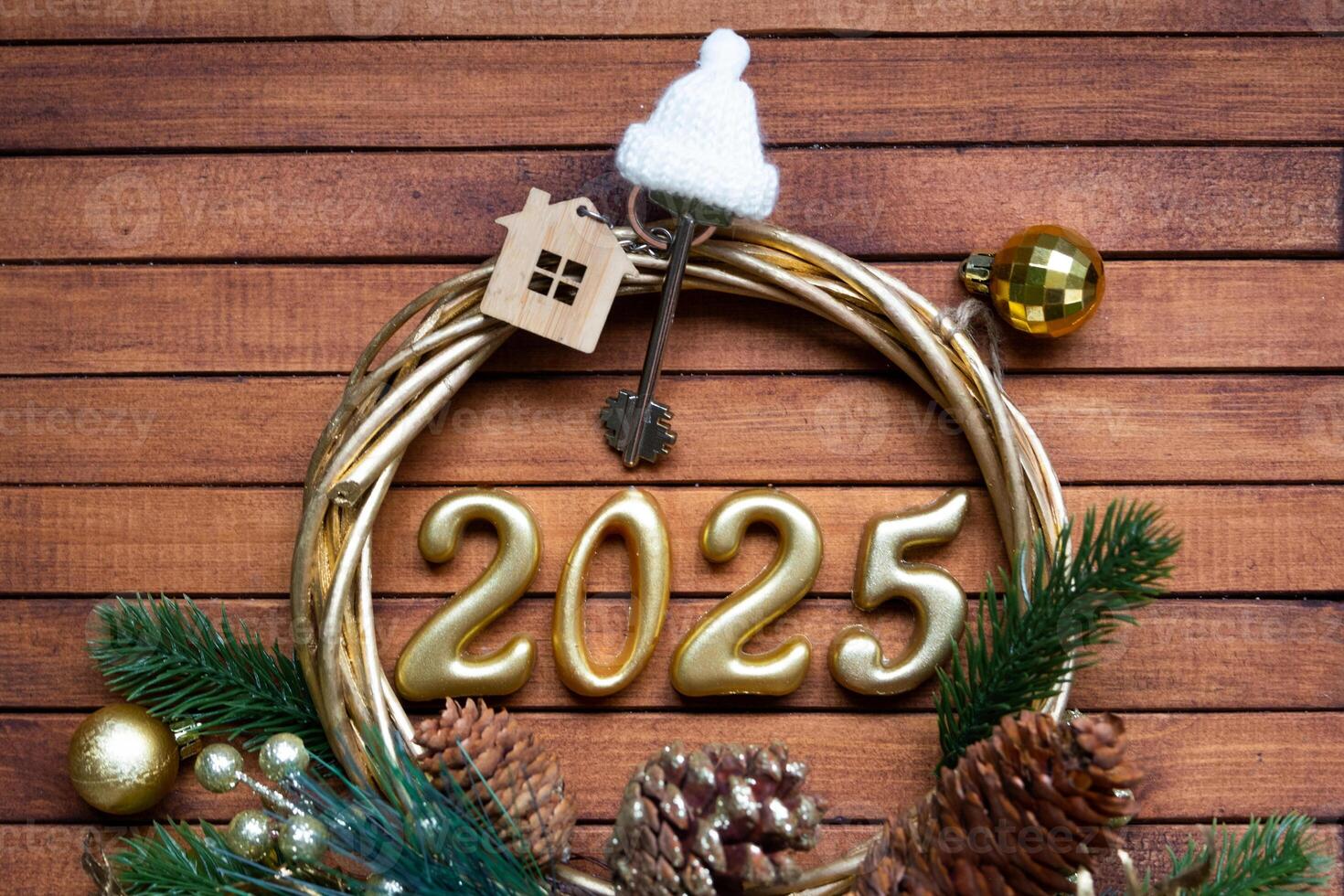 New Year House key with keychain cottage on festive brown wooden background with number 2025 in wreath, lights of garlands. Purchase, construction, relocation, mortgage, insurance photo