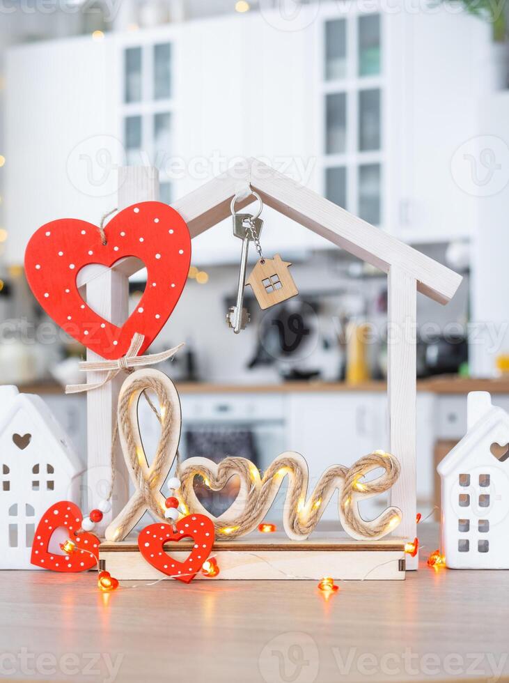 Key to tiny house of cozy home with Valentine decor on table of kitchen. Gift for valentines day, family love nest. design, project, moving to new house, mortgage, rent and purchase real estate photo