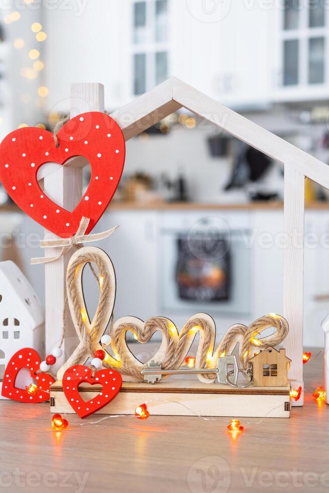 Key to tiny house of cozy home with Valentine decor on table of kitchen. Gift for valentines day, family love nest. design, project, moving to new house, mortgage, rent and purchase real estate photo