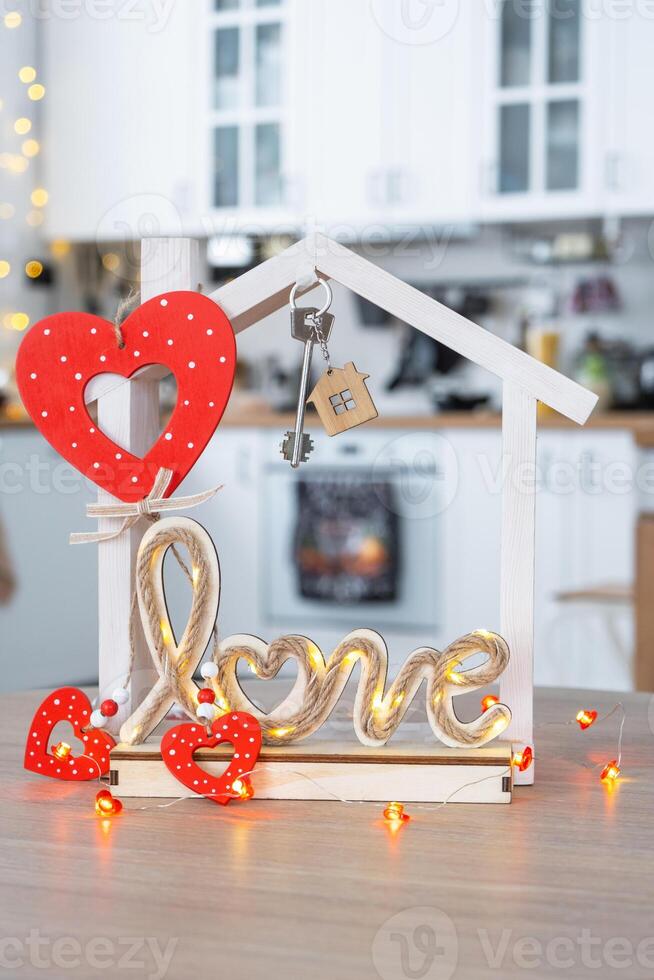 Key to tiny house of cozy home with Valentine decor on table of kitchen. Gift for valentines day, family love nest. design, project, moving to new house, mortgage, rent and purchase real estate photo