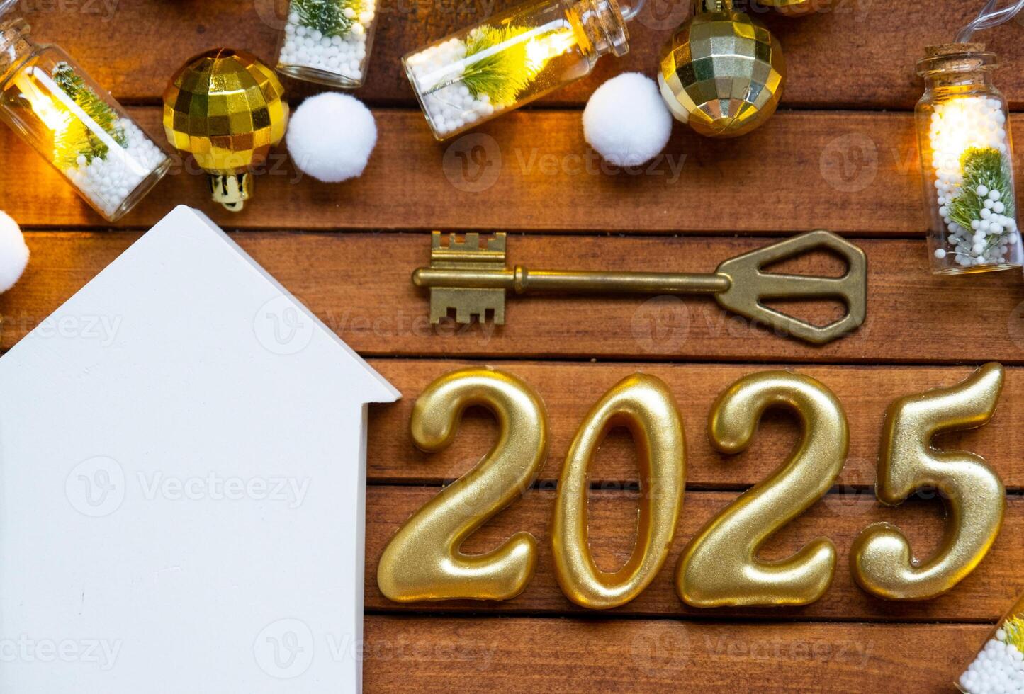 House key with tiny figure of home mock up on festive brown wooden background, lights of garlands. New Year 2025 wooden letters, greeting card. Purchase, construction, relocation, mortgage, insurance photo