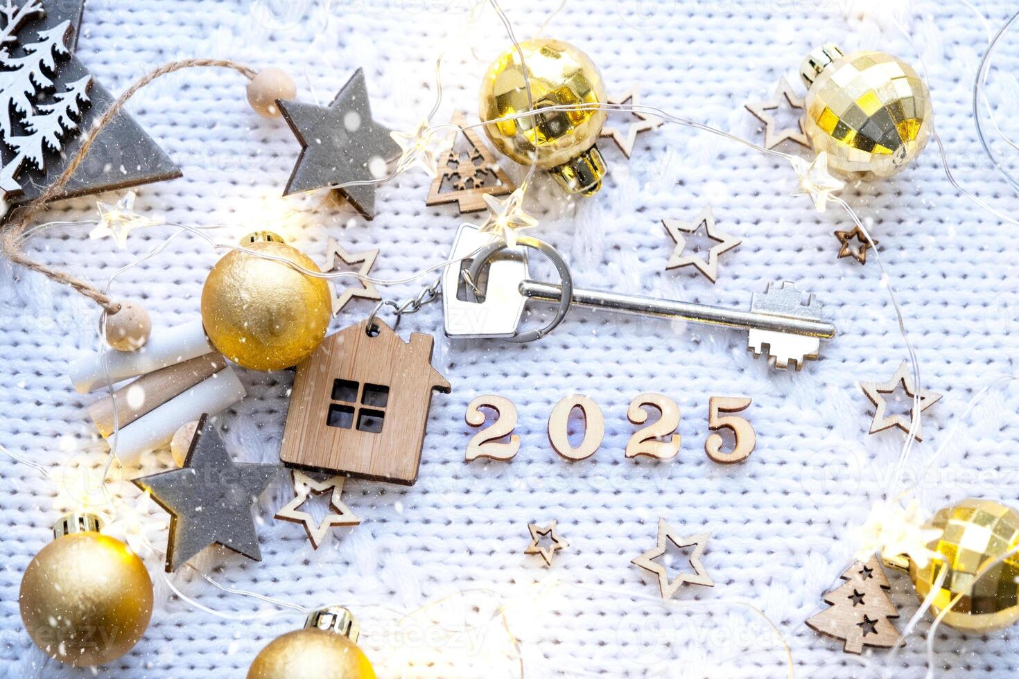 House key with keychain cottage on festive background with stars, lights of garlands. New Year 2025 wooden letters, greeting card. Purchase, construction, relocation, mortgage, insurance photo