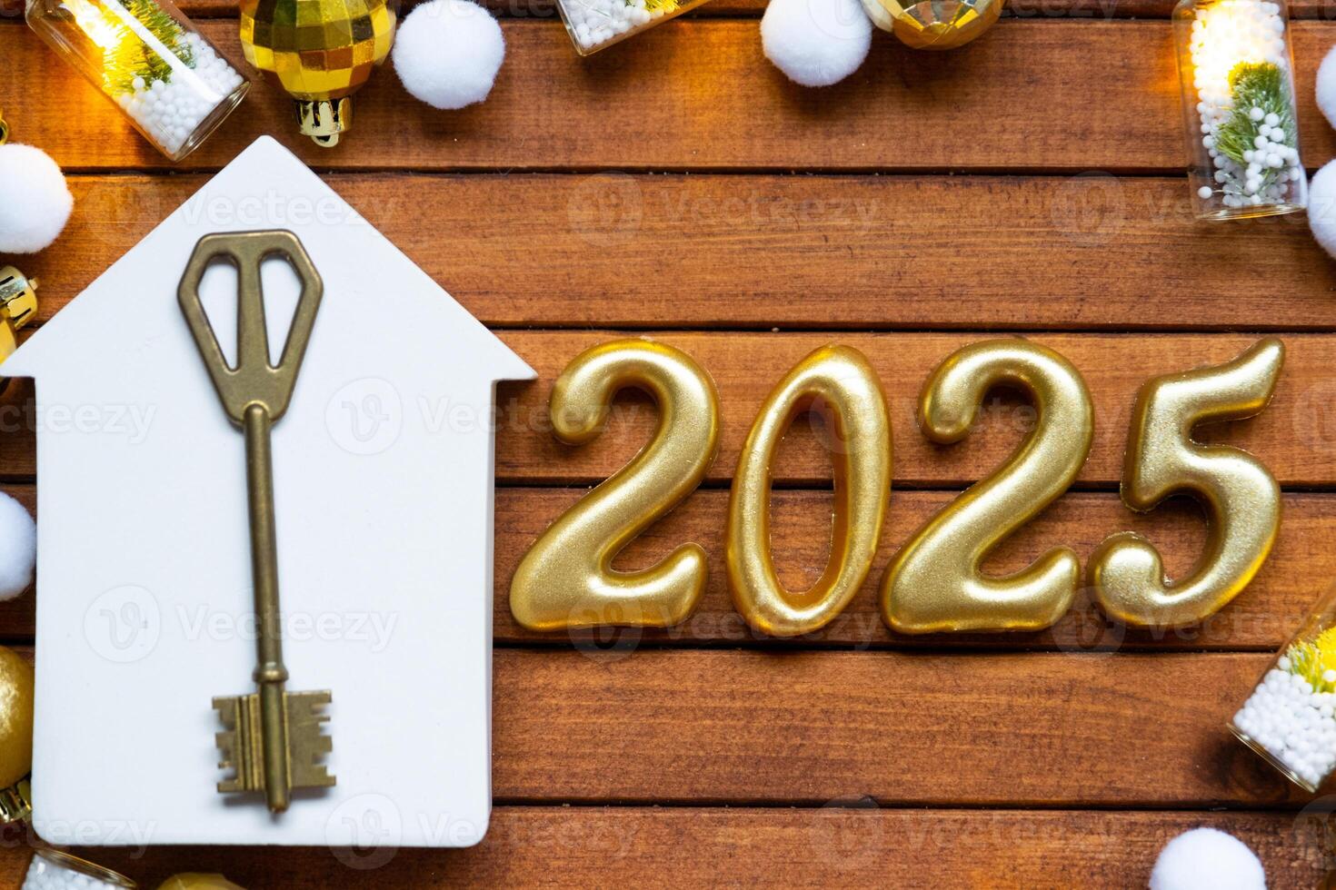 House key with tiny figure of home mock up on festive brown wooden background, lights of garlands. New Year 2025 wooden letters, greeting card. Purchase, construction, relocation, mortgage, insurance photo