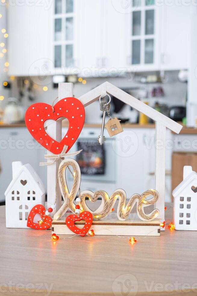 llave a minúsculo casa de acogedor hogar con enamorado decoración en mesa de cocina. regalo para san valentin día, familia amor nido. diseño, proyecto, Moviente a nuevo casa, hipoteca, alquilar y compra real inmuebles foto