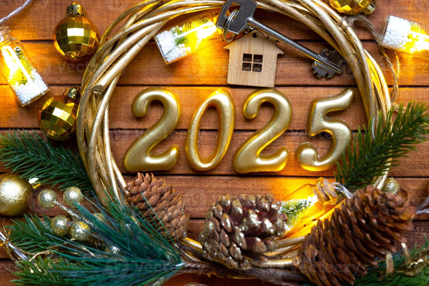 New Year House key with keychain cottage on festive brown wooden background with number 2025 in wreath, lights of garlands. Purchase, construction, relocation, mortgage, insurance photo