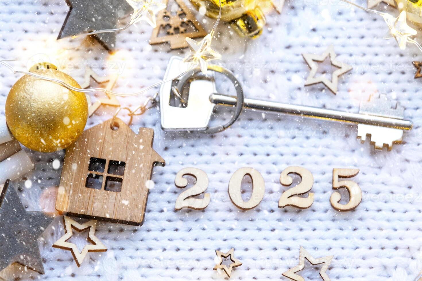 House key with keychain cottage on festive background with stars, lights of garlands. New Year 2025 wooden letters, greeting card. Purchase, construction, relocation, mortgage, insurance photo