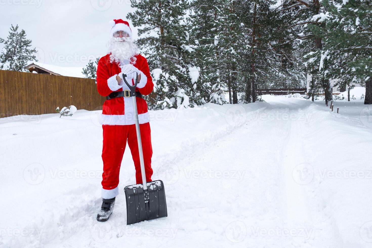 Papa Noel claus limpia nieve con pala en invierno al aire libre después un nevada. limpieza el calles en el aldea, claro el paso para carros, difícil clima condiciones para Navidad y nuevo año foto