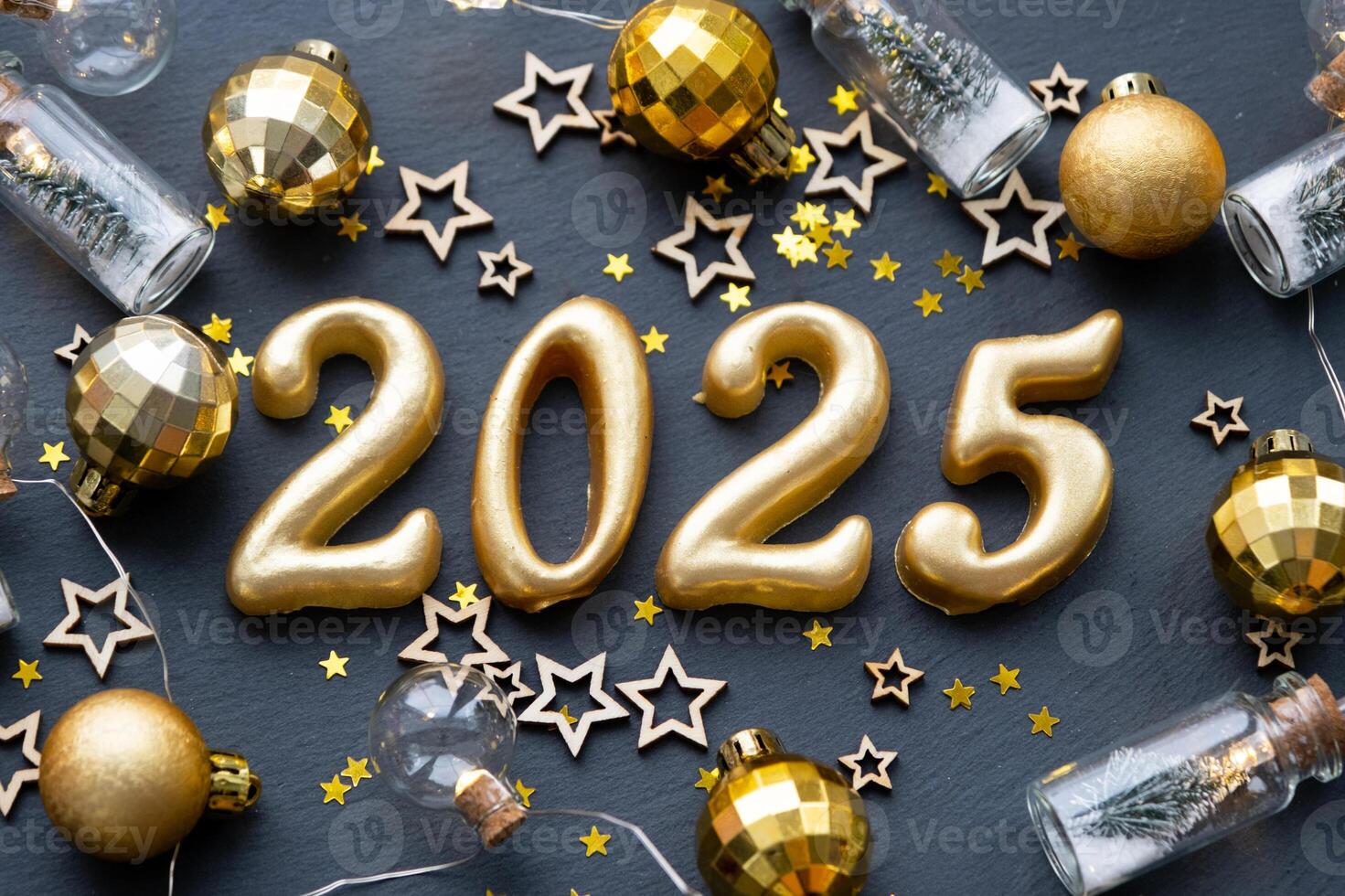 The golden figures 2025 made of candles on a black stone slate background are decorated with a festive decor of stars, sequins, fir branches, balls and garlands. Greeting card, happy New Year. photo